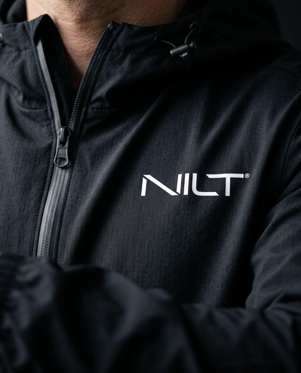 Detalhe do capuz com cordão, do zíper e do logo NILT no corta-vento preto